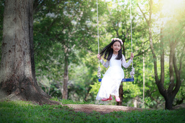 Portrait of little Asian girl playing the swing under the big tree in the nature forest select focus shallow depth of field