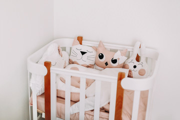 Fototapeta na wymiar Sweet nursery room decorations for a baby girl. Stylish baby room interior with comfortable crib. Cozy children bedroom in scandinavian style with colored decorative pillows.