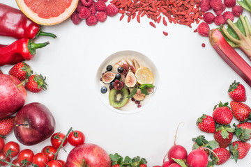 Food frame constructed with red fruits and vegetables and some juicy fruits in the bowl, fresh raw organic garnished on white background. 