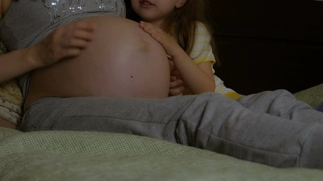 The daughter hugs the pregnant mother's stomach.