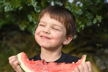 Happy boy eating healthy watermelon in garden. Child with a big slice of watermelon
