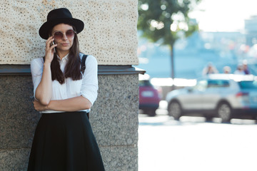 Fototapeta premium young woman in a hat and a white shirt walks in the city and uses a smartphone.