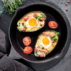 Keto diet dish: Avocado boats with ham cubes, quail eggs, cheese, ingredients around