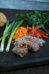 Spring roll with meat and vegetables served on a cutting board. Dark wooden background.