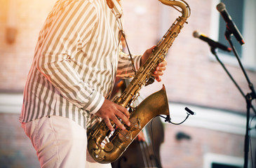 Naklejka premium A skilled jazzman in a striped shirt and white pants performs at a concert with a melody played on a gold saxophone, illuminated by a spotlight.