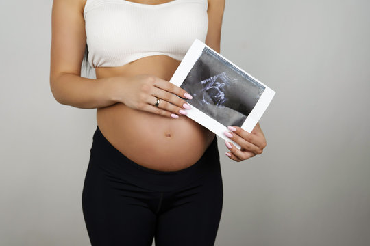 pregnant woman holding ultrasound picture of her baby on isolated white background