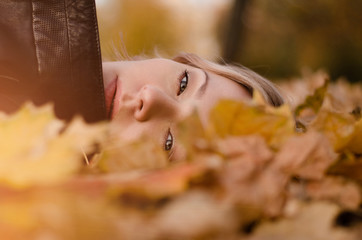 Beautiful woman lying on yellow leaves in park. Leisure time on warm autumn day