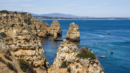Vacation vew of colourful cliffs off Ponta da Piedade headland and cliffs rising from the turquoise waters of the sea. Lagos shore in distance