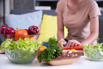 In selective focus of mixed Fresh vegetable bow ,wooden mushroom tray and fruit bowl put on table prepare for cooking,in front of blurred woman hand cutting carrot,blurry light around