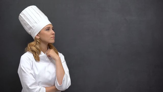 Pensive senior cook touching chin against black board, searching for inspiration
