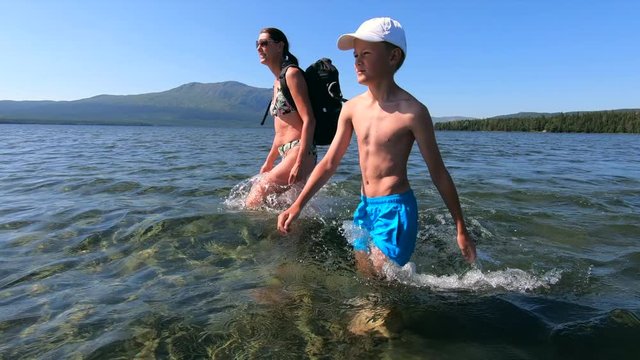 A mother and her son trekking across a shallow part of a mountain lake in Sweden