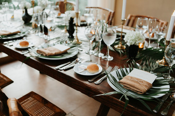 modern and bohemian table decorations at wedding reception, table setting with candle sticks, palm leafs, and flowers