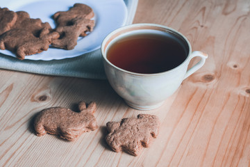 Sweet breakfast, tea break, sweet snack, cup of tea, homemade cookies in the form of a bunny and christmas tree on a wooden table, a white plate with cookies on a napkin