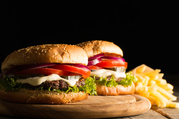 Home made hamburger with beef, onion, tomato, lettuce and cheese. Fresh burger close up on wooden rustic table with potato fries, beer and chips. Cheeseburger.