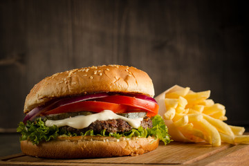 Home made hamburger with beef, onion, tomato, lettuce and cheese. Fresh burger close up on wooden rustic table with potato fries, beer and chips. Cheeseburger.