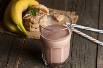 Photo of fresh Made Chocolate Banana Smoothie on a wooden table with cookies, banana and coconut. Milkshake. Protein diet. Healthy food concept.