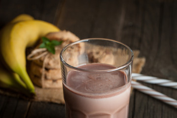 Photo of fresh Made Chocolate Banana Smoothie on a wooden table with cookies, banana and coconut. Milkshake. Protein diet. Healthy food concept.
