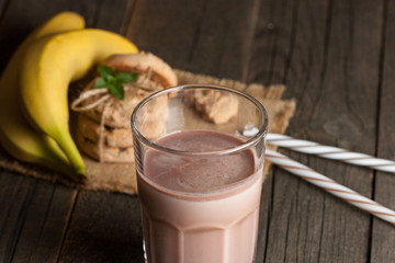 Photo of fresh Made Chocolate Banana Smoothie on a wooden table with cookies, banana and coconut. Milkshake. Protein diet. Healthy food concept.