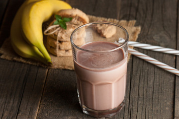 Photo of fresh Made Chocolate Banana Smoothie on a wooden table with cookies, banana and coconut. Milkshake. Protein diet. Healthy food concept.