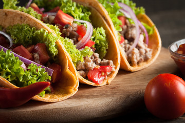 Photo of Mexican tacos with ground beef, onion, tomatoes, chili, red sauce, lettuce and lime on wooden background. Spicy and fast food concept.