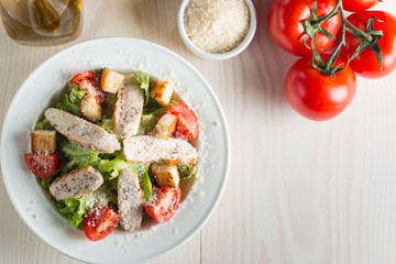 Fresh salad with delicious chicken breast, ruccola, spinach, cabbage, arugula and tomato on wooden background. Oil, salt and pepper.