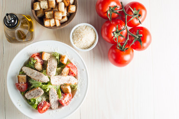 Fresh salad with delicious chicken breast, ruccola, spinach, cabbage, arugula and tomato on wooden background. Oil, salt and pepper.