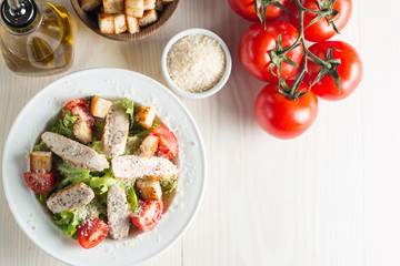 Fresh salad with delicious chicken breast, ruccola, spinach, cabbage, arugula and tomato on wooden background. Oil, salt and pepper.