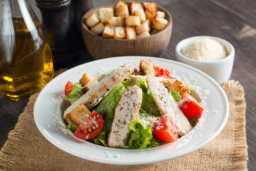 Fresh salad with delicious chicken breast, ruccola, spinach, cabbage, arugula and tomato on wooden background. Oil, salt and pepper.