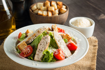 Fresh salad with delicious chicken breast, ruccola, spinach, cabbage, arugula and tomato on wooden background. Oil, salt and pepper.