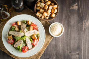 Fresh salad with delicious chicken breast, ruccola, spinach, cabbage, arugula and tomato on wooden background. Oil, salt and pepper.