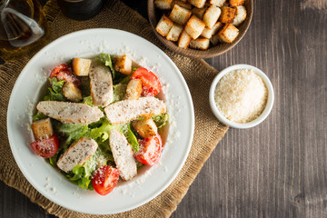 Fresh salad with delicious chicken breast, ruccola, spinach, cabbage, arugula and tomato on wooden background. Oil, salt and pepper.