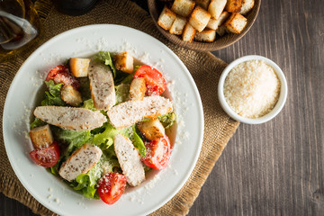 Fresh salad with delicious chicken breast, ruccola, spinach, cabbage, arugula and tomato on wooden background. Oil, salt and pepper.