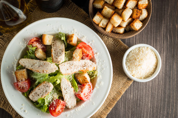 Fresh salad with delicious chicken breast, ruccola, spinach, cabbage, arugula and tomato on wooden background. Oil, salt and pepper.