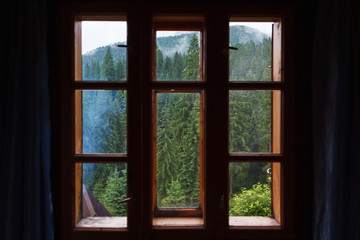 Through the wooden window of the room is visible mountain forest.