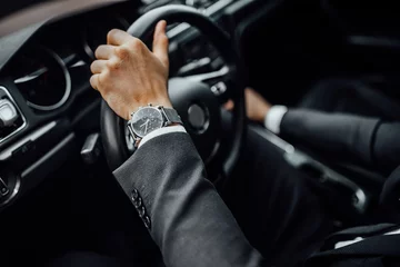 Foto op Plexiglas Close up top view of  man's watch in black suit keeping hand on the steering wheel while driving a luxury car. © Тарас Нагирняк