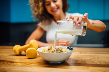 Portrait of young smiling woman eating muesli or cornflakes, milk in bowl.