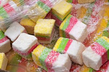 The oriental sweet in Turkish pleases with red, green, yellow and white rolls with coconut. Closeup of turkish sweets at the market, selective focus.