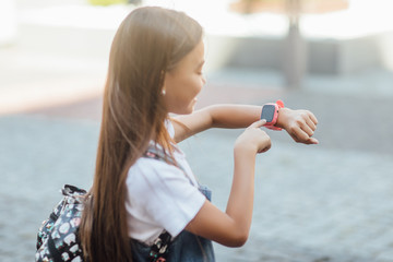 Technology concept for children, a girl wearing jeans dress uses a smartwatch on fresh air. Lifestyle.