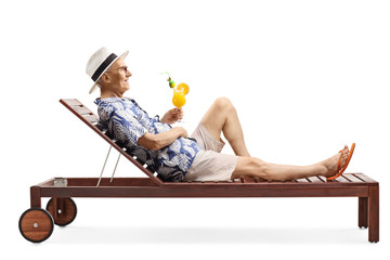Senior man relaxing on a beach bed with a cocktail