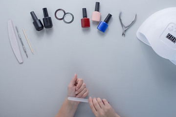 Female hands file nails on light gray background. Nearby are laid out accessories for manicure nail polish, nail files, nippers and personal care. Free space for text. Regular beauty routine for women