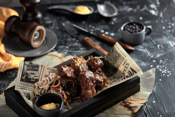 Tasty grilled ribs seasoned with spicy sauce and chopped fresh vegetables on an old rustic wooden cutting board with mustard