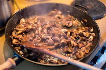 Cooking Champignons mushroom with wooden flipper a stir in pan
