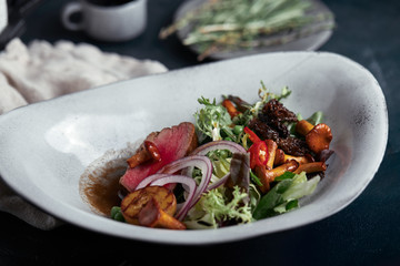 beef tagliata with vegetables. Close-up, low key, gray background.