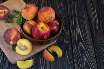 Naklejka na ściany i meble Delicious juicy orange-red peaches and nectarines on a dark background in a clay bowl. Dark background, still life of ripe summer fruits on a brown wooden table. photo with space for text