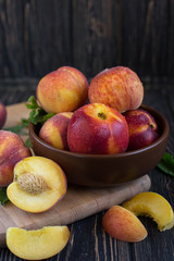 Delicious juicy orange-red peaches and nectarines on a dark background in a clay bowl. Dark background, still life of ripe summer fruits on a brown wooden table. Vertical photo