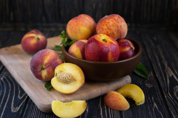 Naklejka na ściany i meble Delicious juicy orange-red peaches and nectarines on a dark background in a clay bowl. Dark background, still life of ripe summer fruits on a brown wooden table.