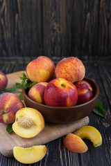 Delicious juicy orange-red peaches and nectarines on a dark background in a clay bowl. Dark background, still life of ripe summer fruits on a brown wooden table. Vertical photo with space for text