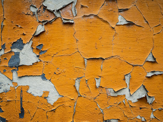 Many layers of paint on the old wall. Peeling orange paint on the wall
