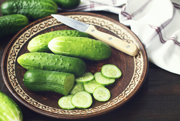 whole and sliced fresh green cucumbers in a close-up plate. background with green cucumbers on the table.