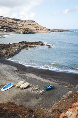 Fototapeta na wymiar Boats on the black sand beach on the rocky point of El Golfo - Lanzarote, Spain